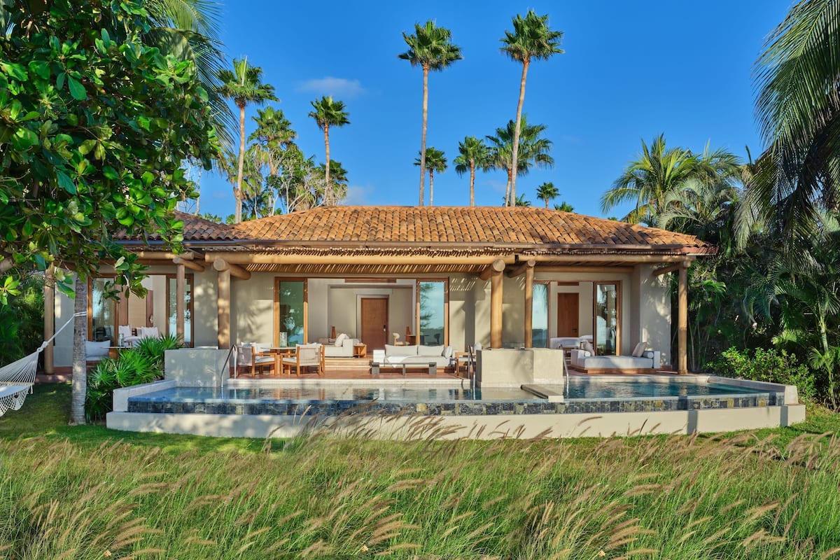 Una casa moderna con piscina, rodeada de palmeras y follaje.