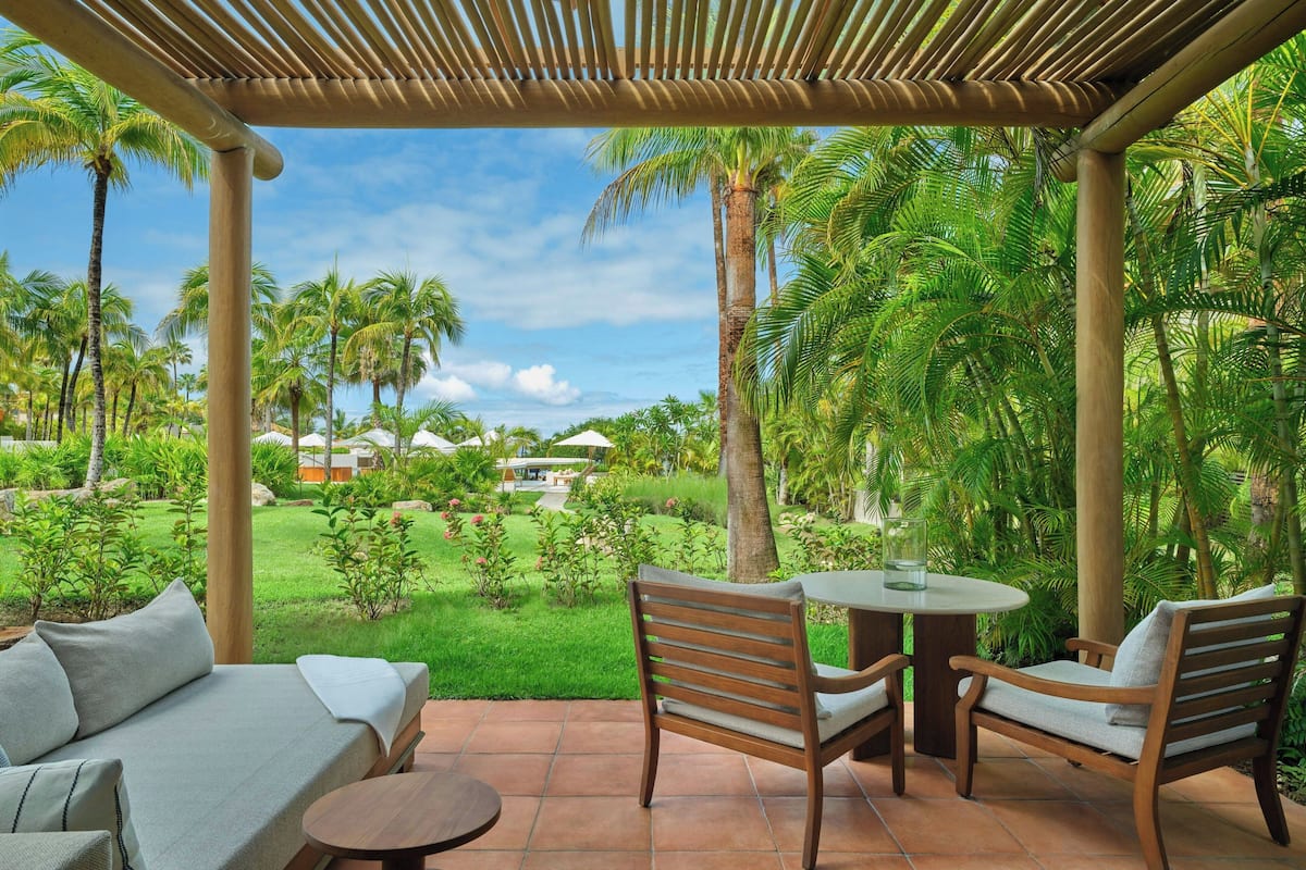 Un espacio de estar al aire libre cubierto con un sofá y sillas, con vistas a un exuberante jardín con palmeras.