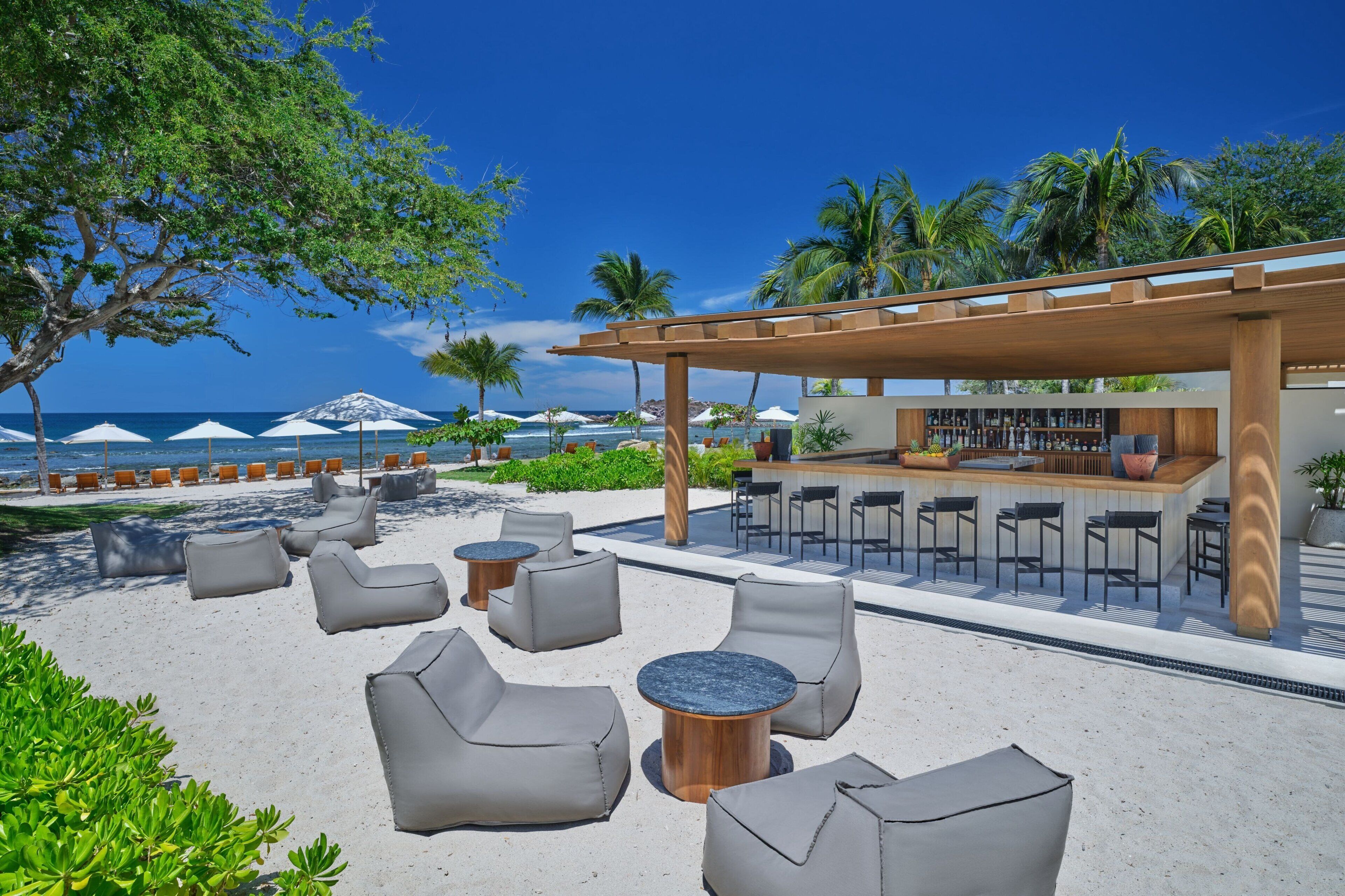 A beachside lounge with outdoor seating, a bar, and a view of the ocean.