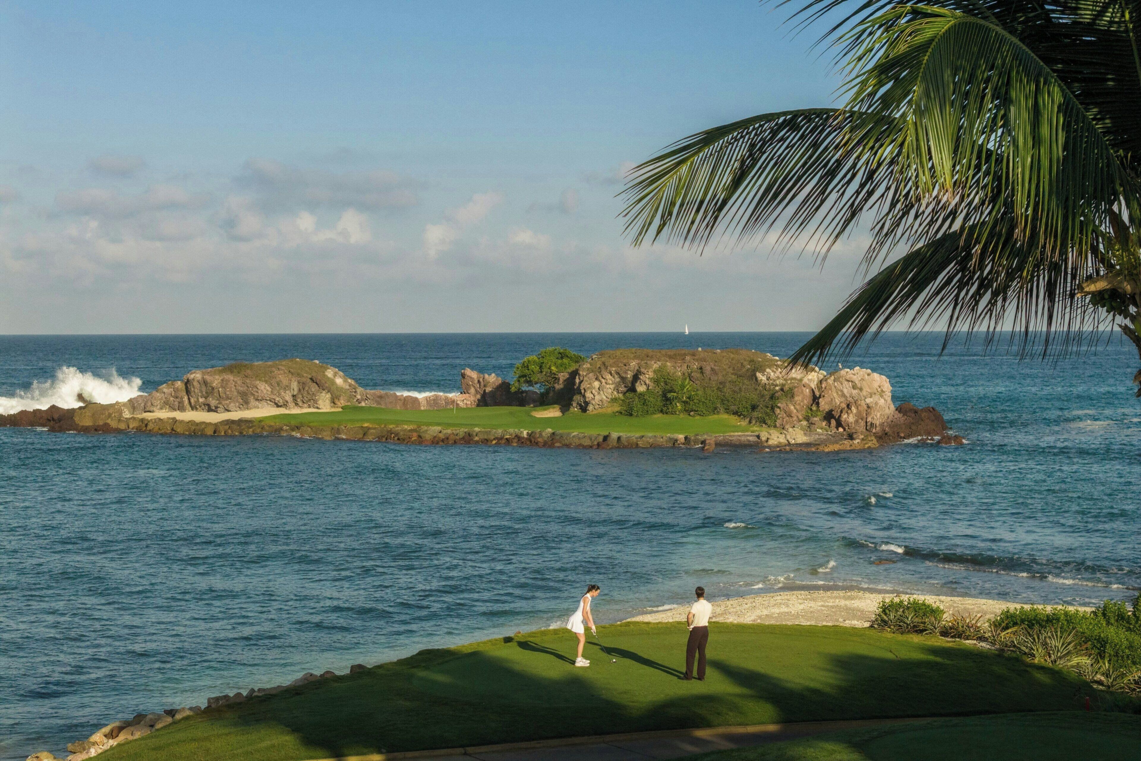 A coastal golf course with a view of the ocean and a lighthouse in the distance.