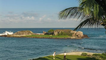 A coastal golf course with a view of the ocean and a lighthouse in the distance.