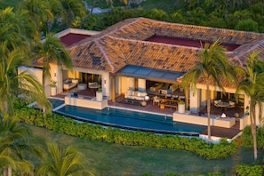 Una casa moderna con piscina, mobiliario exterior y abundante vegetación.
