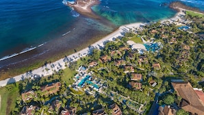 Luchtbeeld van een kustresort met strand, zwembad en weelderige begroeiing.