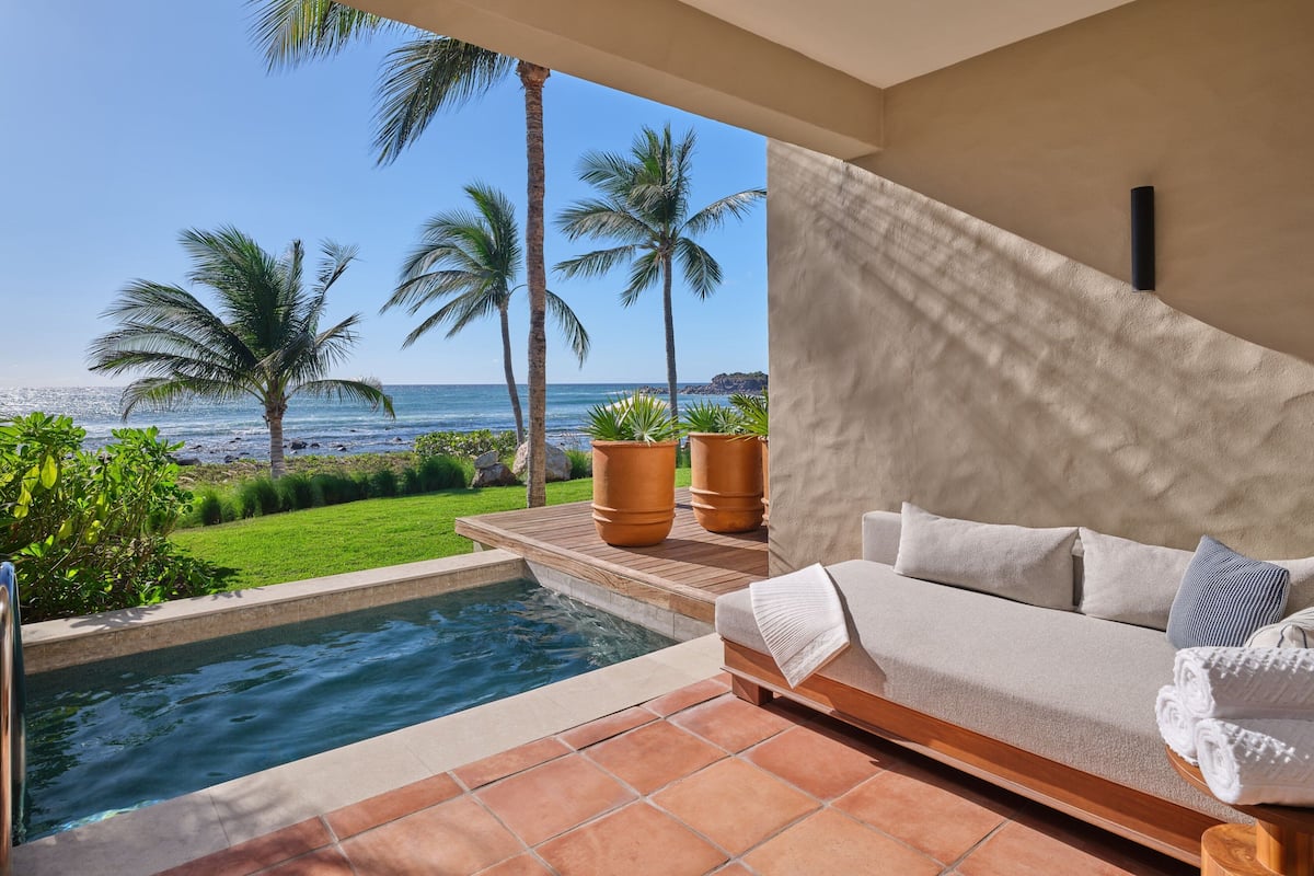 Zona de piscina con vista al océano, un sofá blanco y plantas en macetas.