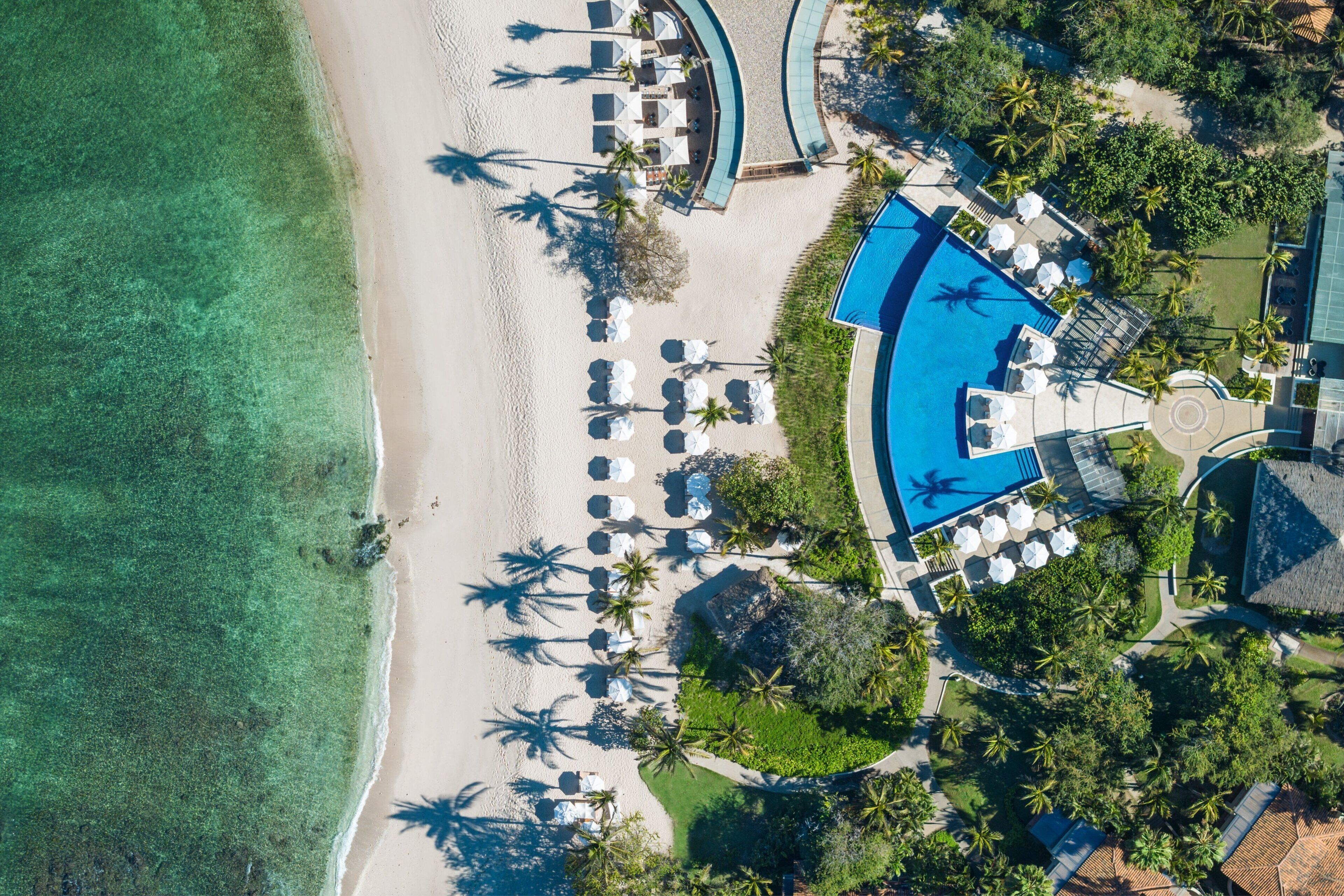 Luftaufnahme eines Resorts mit Strand, Pool und Palmen.