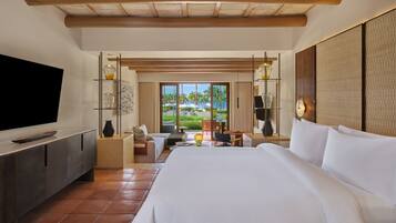 A hotel room with a large bed, a TV, a desk with a chair, and a view of palm trees through the window.