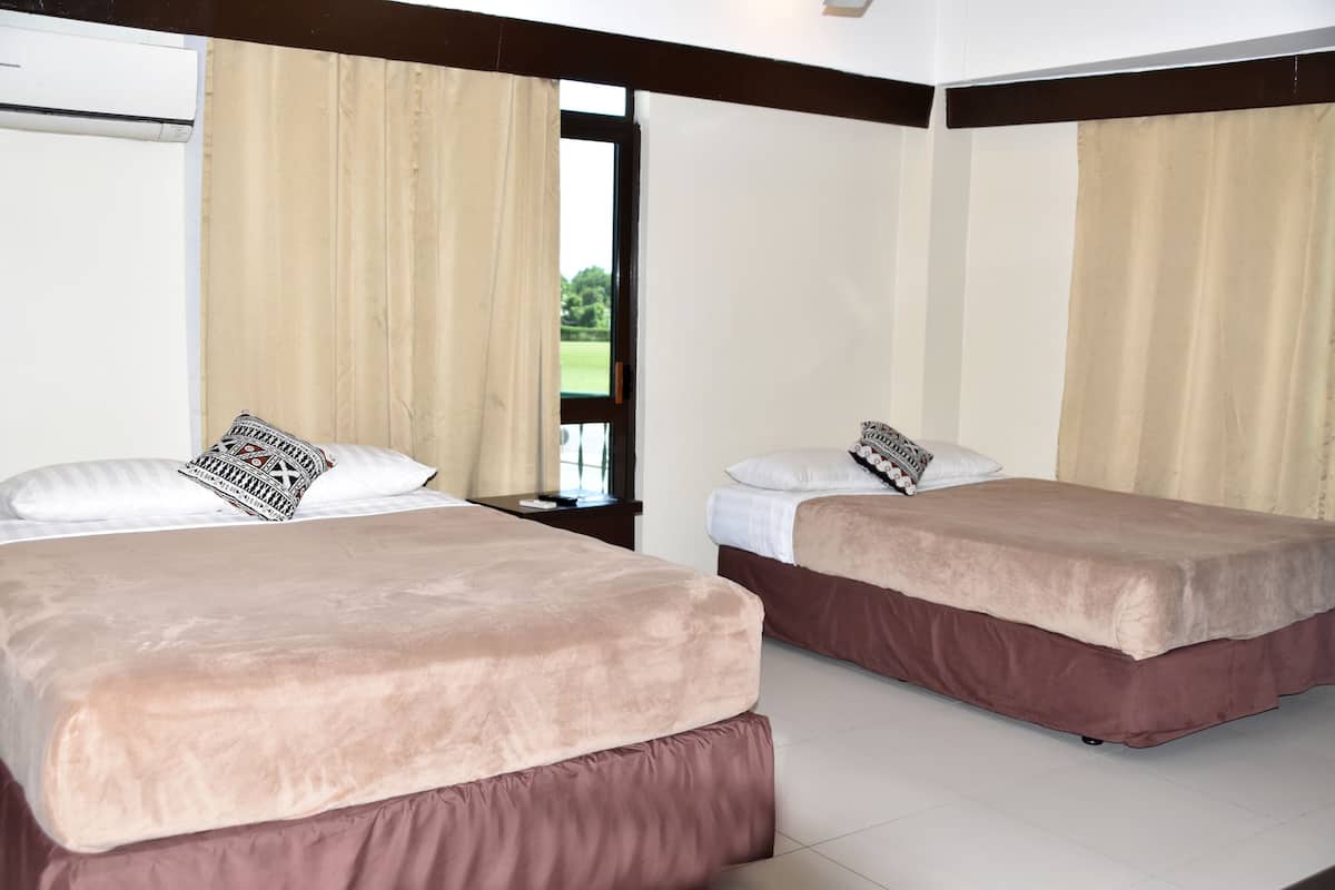 Habitación de hotel con dos camas, cortinas color crema, ventanal con vistas a vegetación y un aire acondicionado blanco.