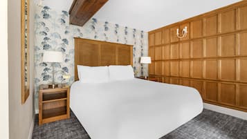 A bedroom with a large bed, wooden headboard, two bedside tables with lamps, and a patterned wallpaper.