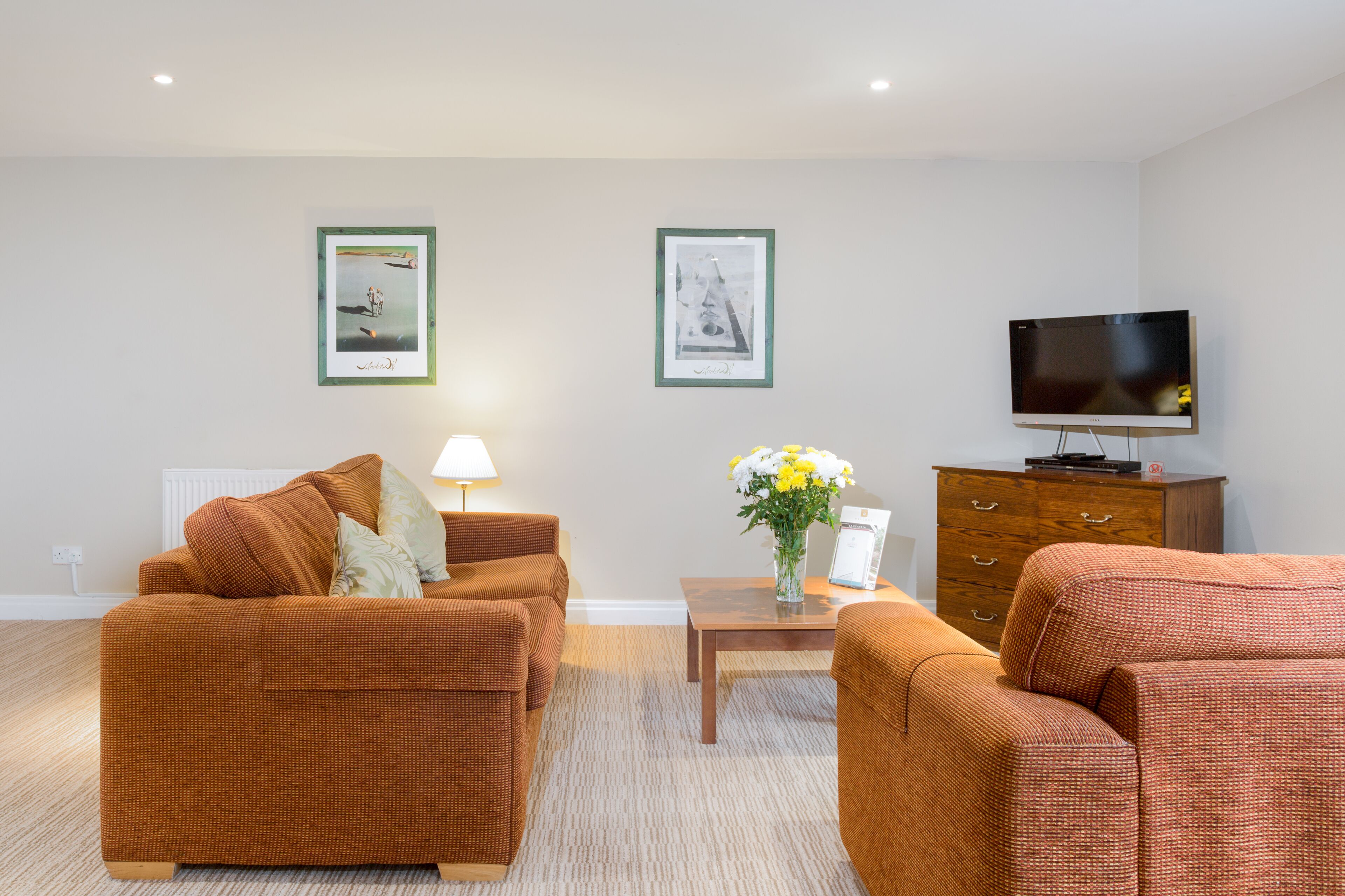 A living room with two brown sofas, a coffee table, a TV, and framed pictures on the wall.