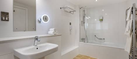 Un baño moderno con lavamanos, espejo y ducha con mampara de vidrio.