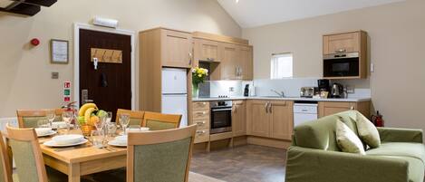 A modern kitchen with wooden cabinets, a dining area with a table set for four, and a green sofa.