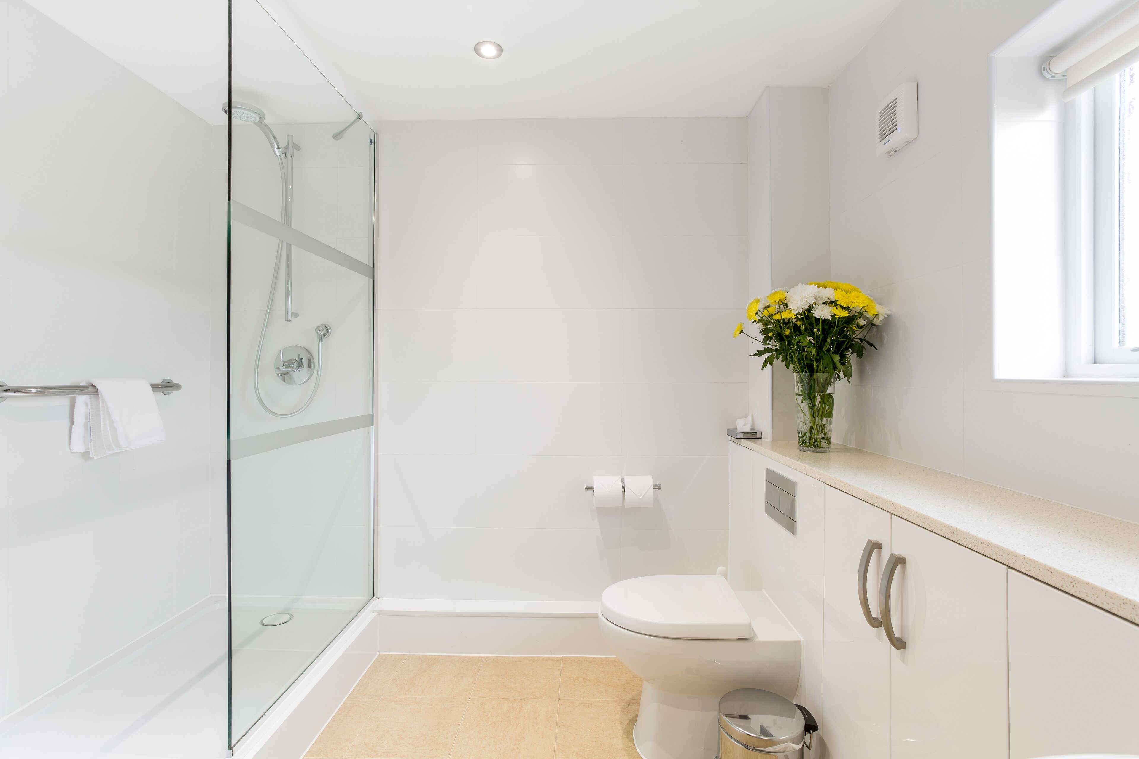 A modern bathroom with a glass-enclosed shower, a toilet, and a sink with a vase of flowers.