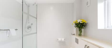 A modern bathroom with a glass-enclosed shower, a toilet, and a sink with a vase of flowers.