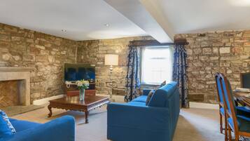 Una sala de estar con pared de piedra, chimenea, sofá y televisor.