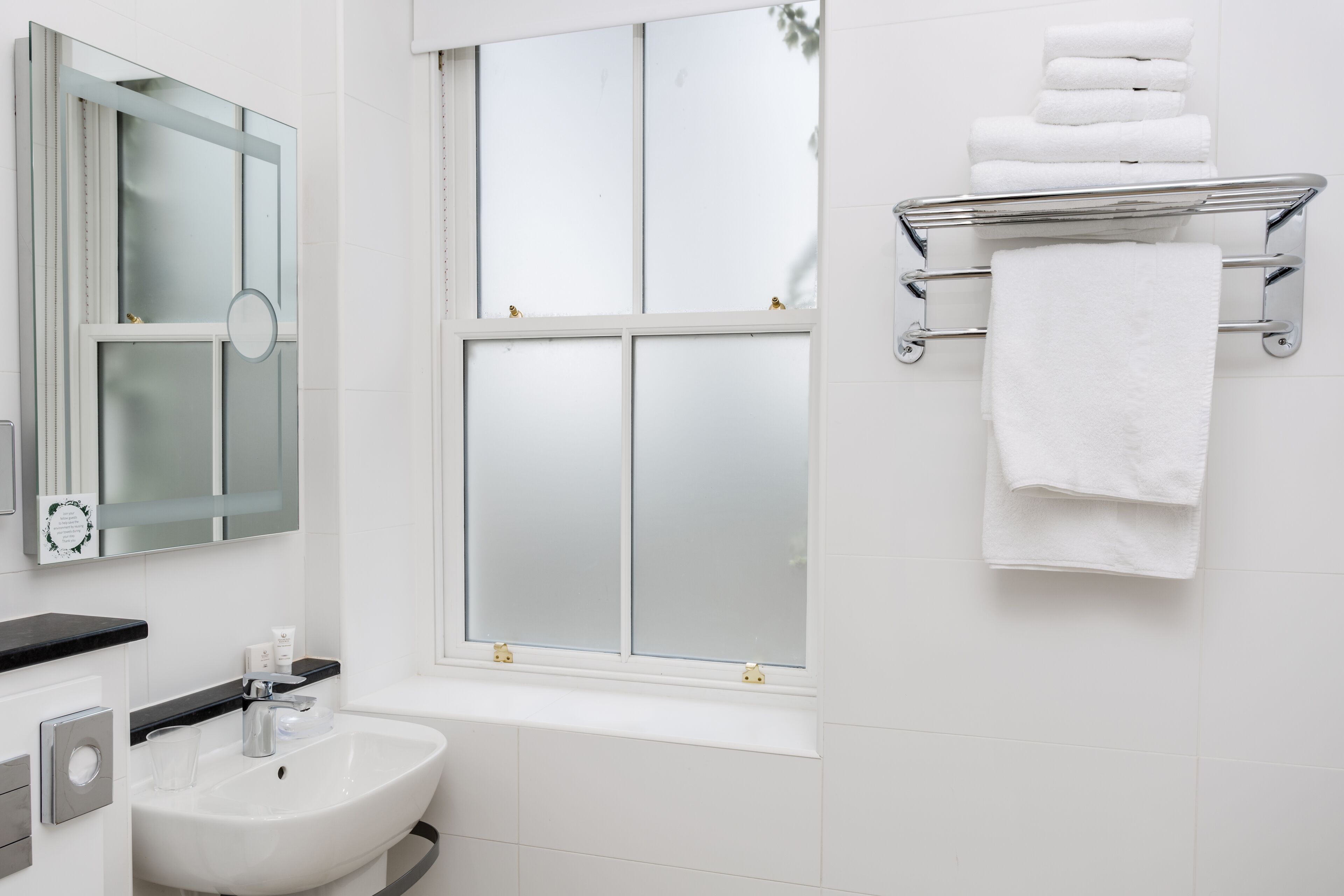 A bathroom with a white sink, mirror, and window.