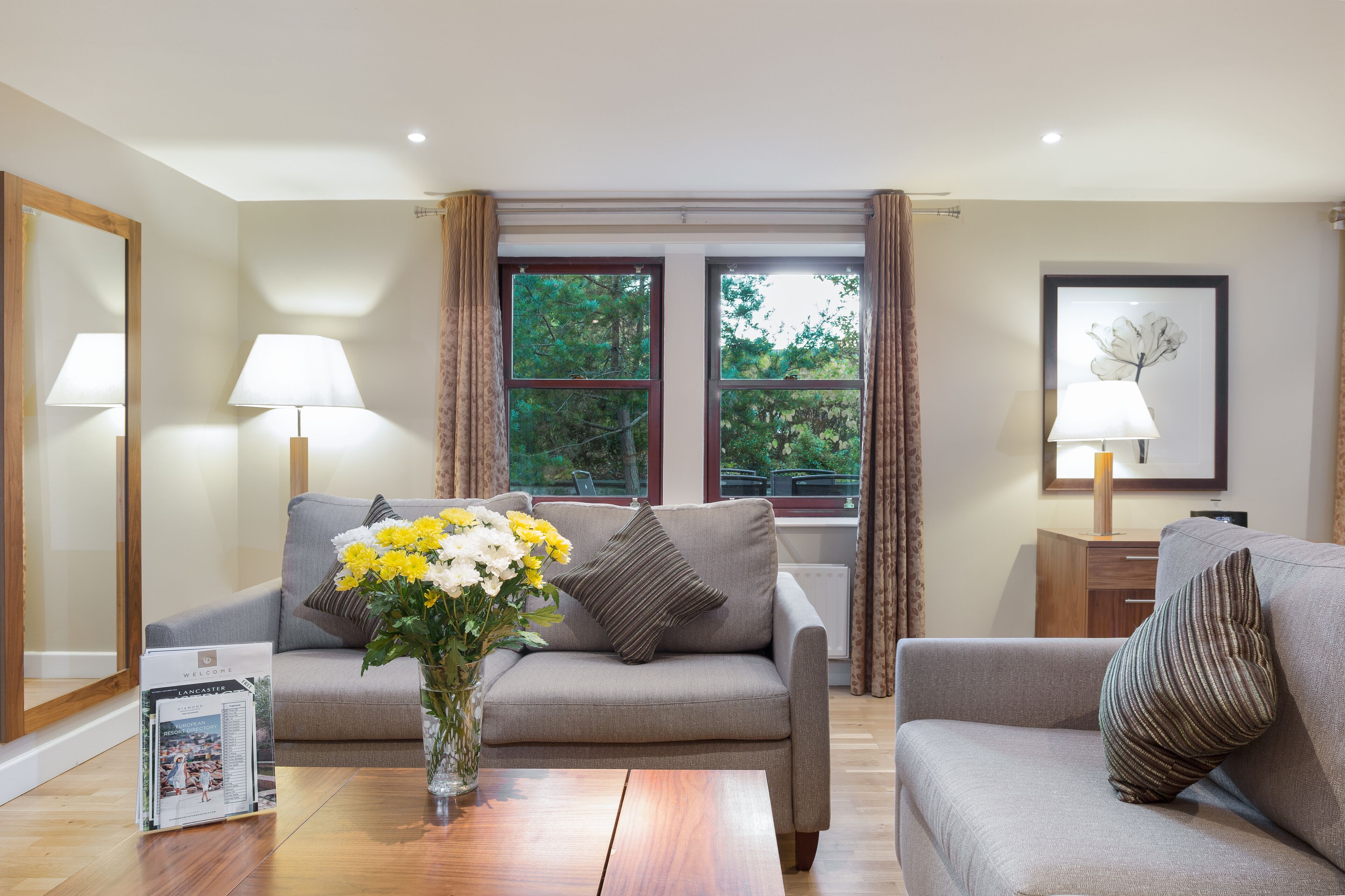 Una sala de estar con un sofá, una mesita de centro con un jarrón de flores y una ventana con cortinas.