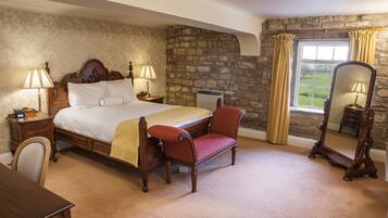 A bedroom with a large bed, two bedside tables, a chair, a mirror, and a stone wall.