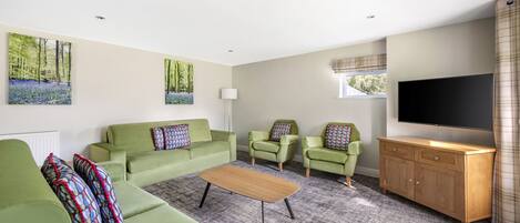 A modern living room with green sofas, a wooden coffee table, and a flat-screen TV.