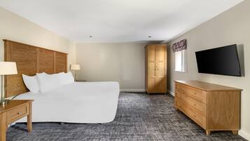 Une chambre d’hôtel avec un grand lit, une tête de lit en bois, une commode, un téléviseur et une armoire.