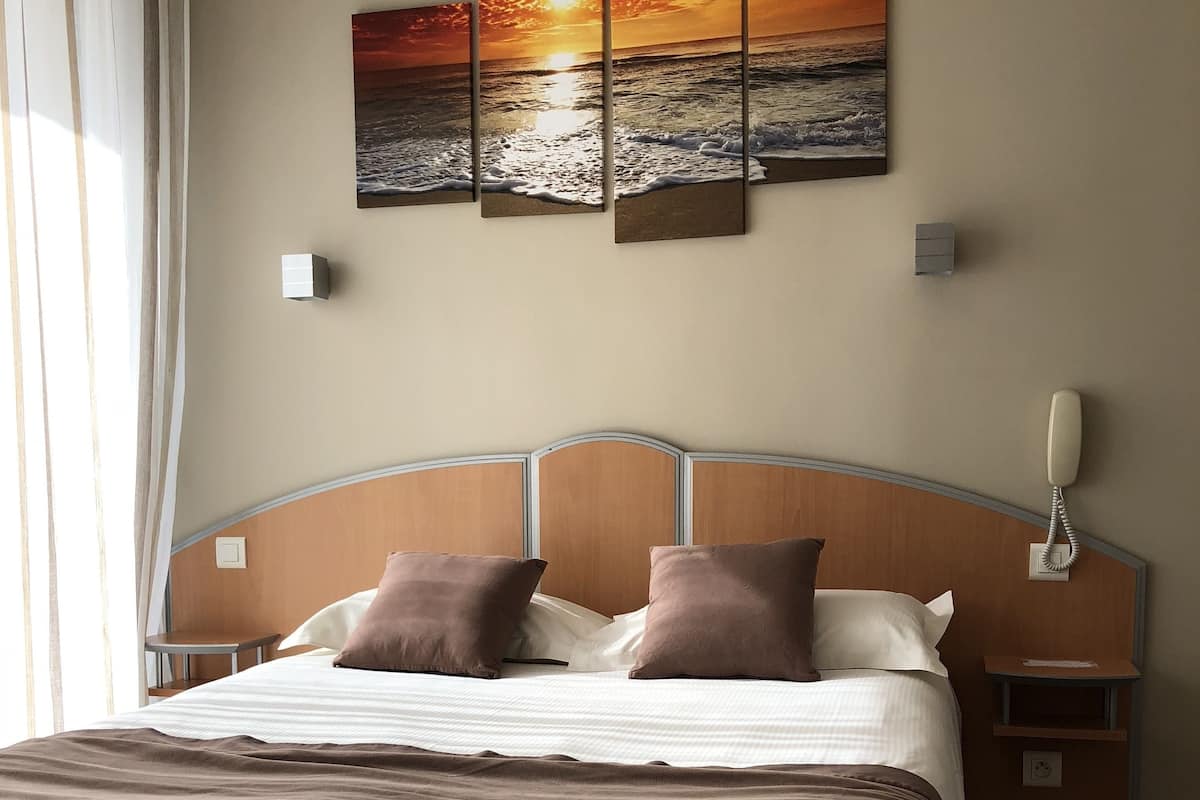 Un letto rifatto con cura, una coperta marrone, una testiera e due comodini con lampade.