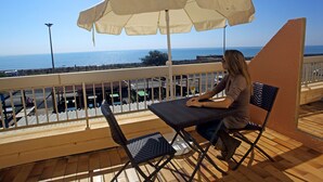 Un balcón con una mesa, sillas y un gran parasol, con vista al mar.