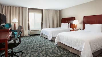 A hotel room with two beds, a desk with a chair, a TV, and a window with curtains.