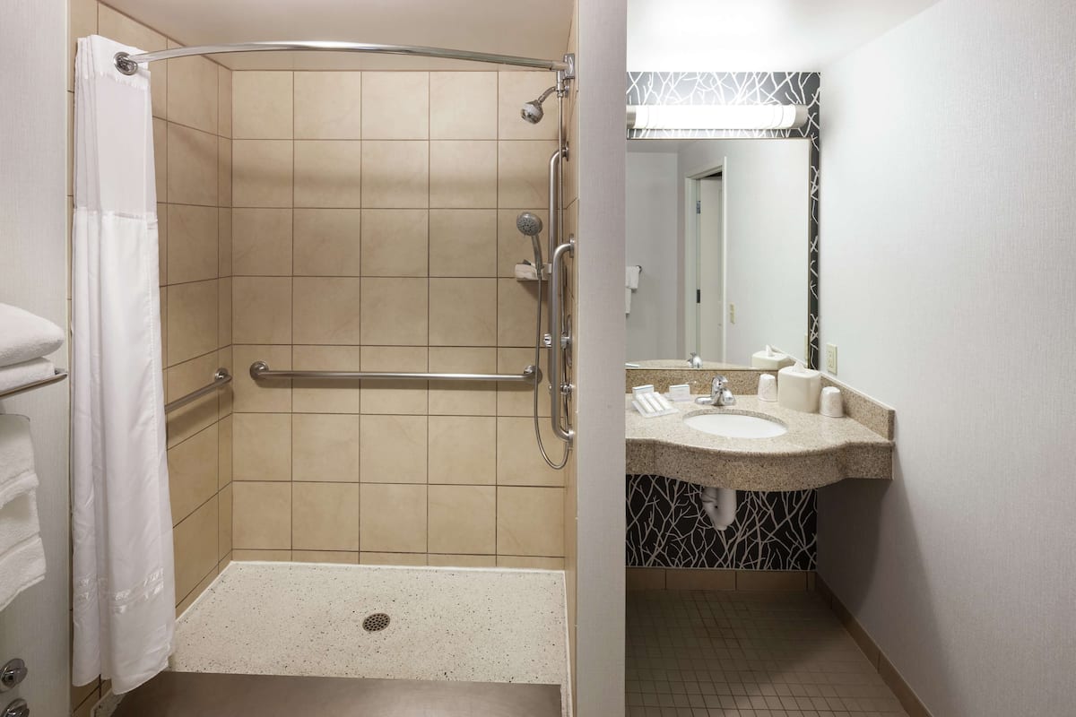 A shower with a grab bar, a sink with a mirror, and a towel rack.
