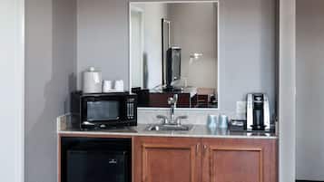 Uma cozinha compacta de hotel, com micro-ondas, cafeteira, pia e pequena geladeira.
