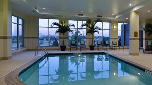 Una piscina interior con ventanales, sillas y plantas en macetas.