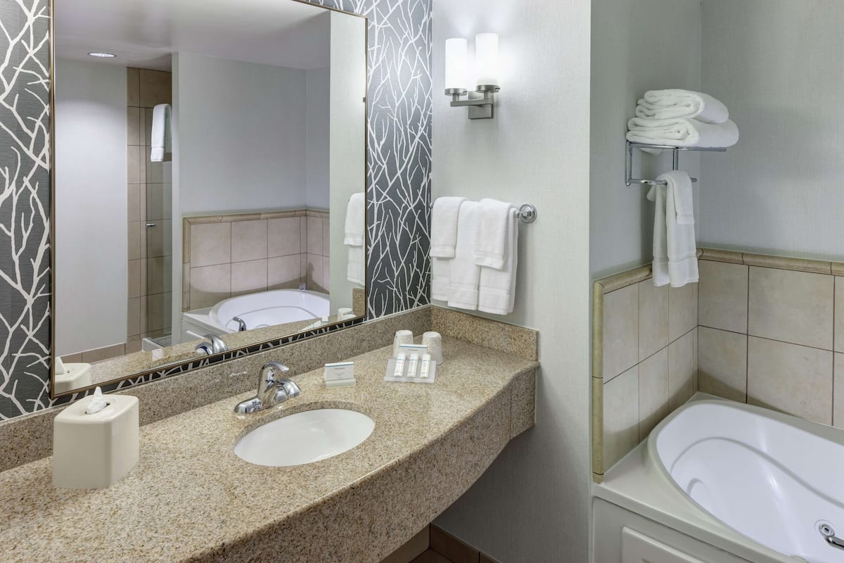 A modern bathroom with a granite countertop, a sink, a mirror, a towel rack, and a bathtub.