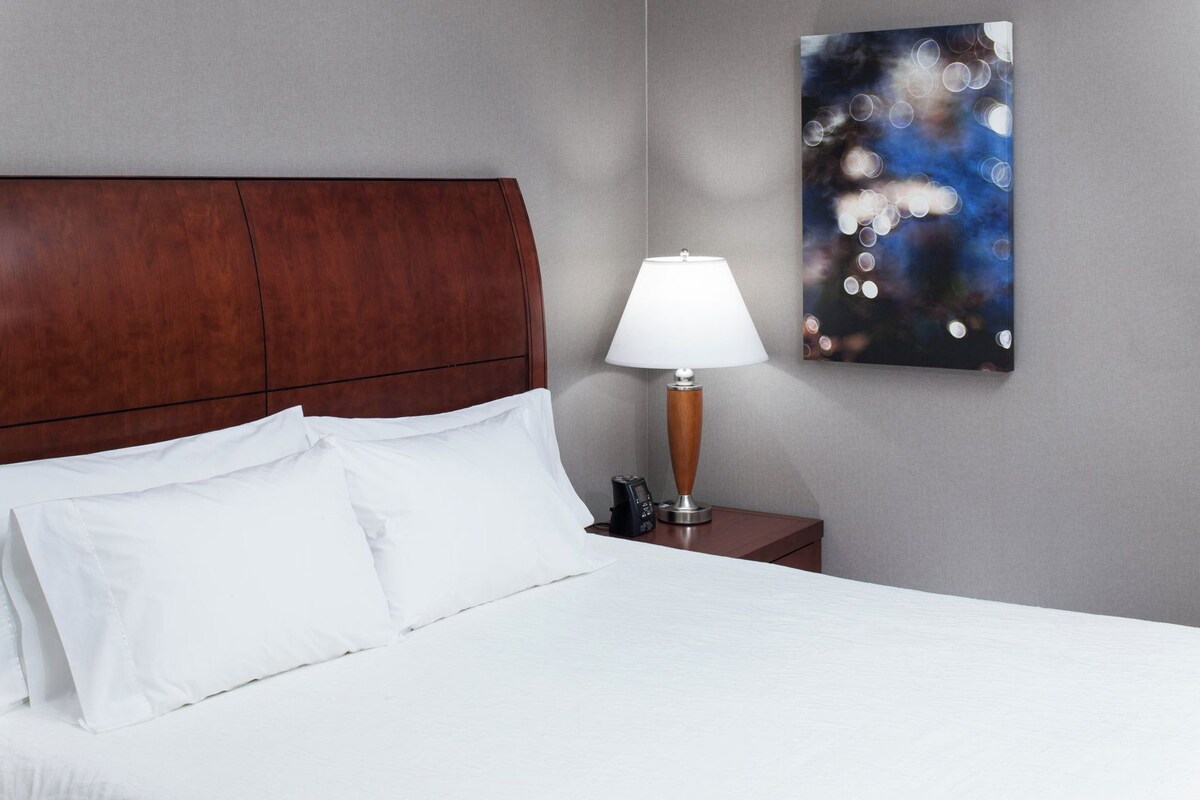 A neatly made bed with white linens, a wooden headboard, and a bedside table with a lamp and a phone.
