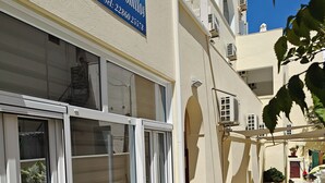 A hotel exterior with a sign reading "Villa Aenemorilos," outdoor seating with chairs and a table, and a tiled patio area. - Anemomilos Villa (Santorini)