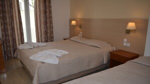 A hotel room with two beds, a nightstand, and a window with curtains. - Anemomilos Villa (Santorini)