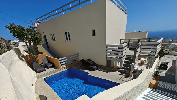 A modern building with a rooftop pool, outdoor seating, and a view of the sea. - Anemomilos Villa (Santorini)