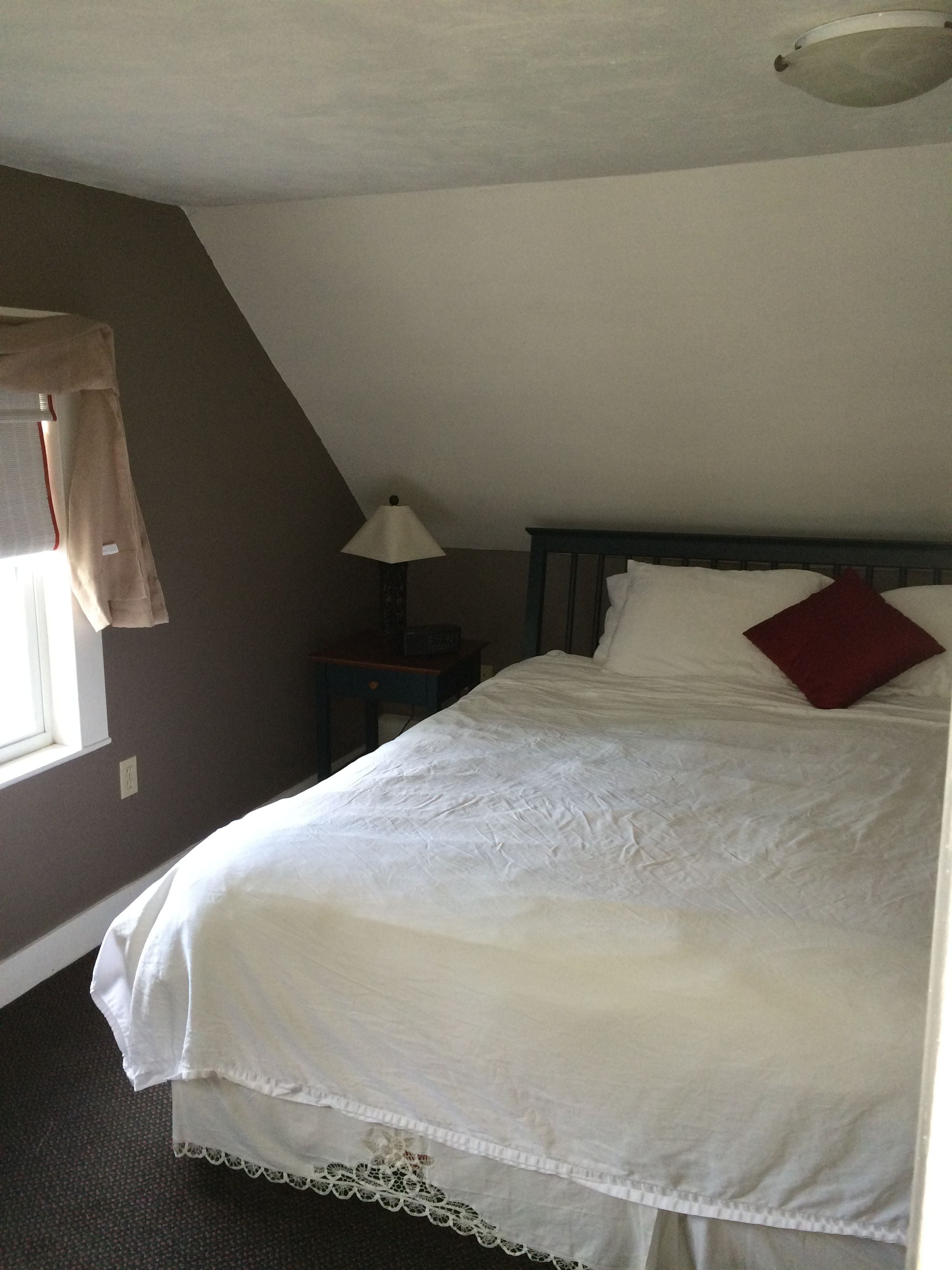 A bedroom with a bed, a nightstand, a lamp, and a window with curtains.