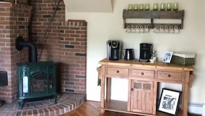 Una habitación rústica con chimenea de ladrillo, un mueble de madera con cafetera y un zapatero en la pared.