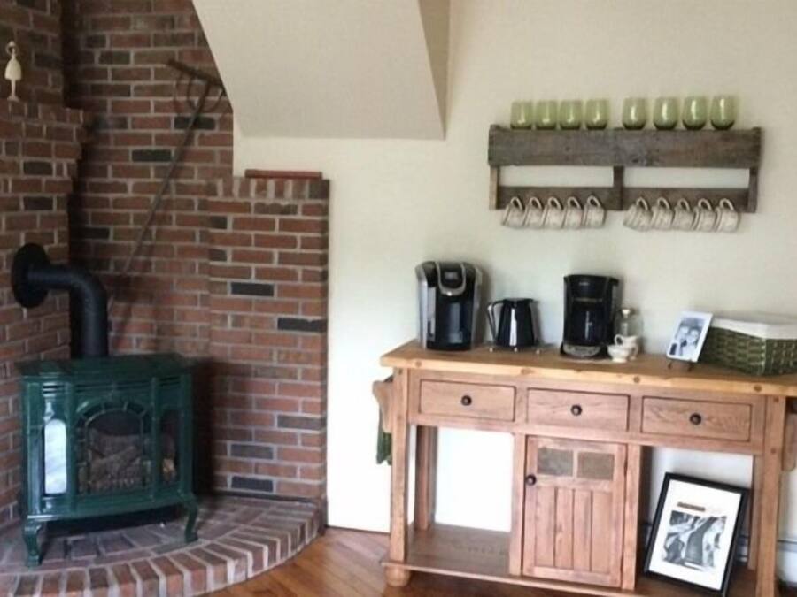 A rustic room with a brick fireplace, a wooden cabinet with a coffee maker, and a wall-mounted shoe rack.