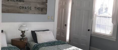 A room with two beds, a motivational quote on the wall, a lamp, and a window with a view of a building.
