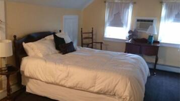 A bedroom with a bed, a chair, a nightstand, and a window with curtains.