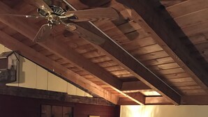 Un dormitorio con techo de madera, una cama con edredón blanco, una mesita de noche con lámpara y un aparador.