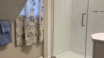 A modern bathroom with a glass shower enclosure, a white tiled shower area, a wooden floor, and a towel hanging on the wall.