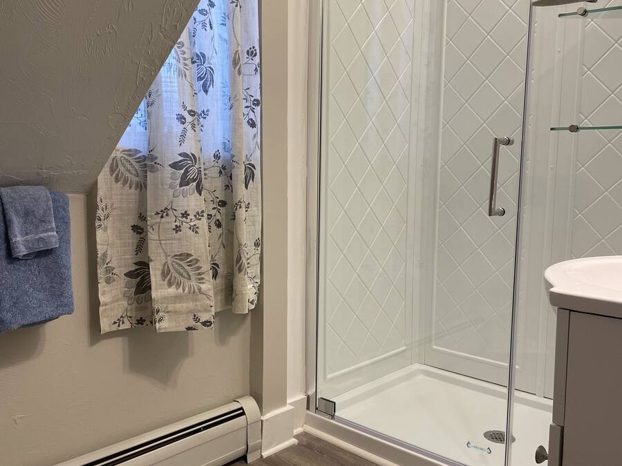 Une salle de bain moderne avec une douche à parois de verre, un espace de douche carrelé de blanc, un plancher en bois et une serviette accrochée au mur.