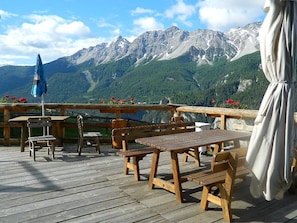 A wooden deck with tables and chairs, overlooking a mountainous landscape.