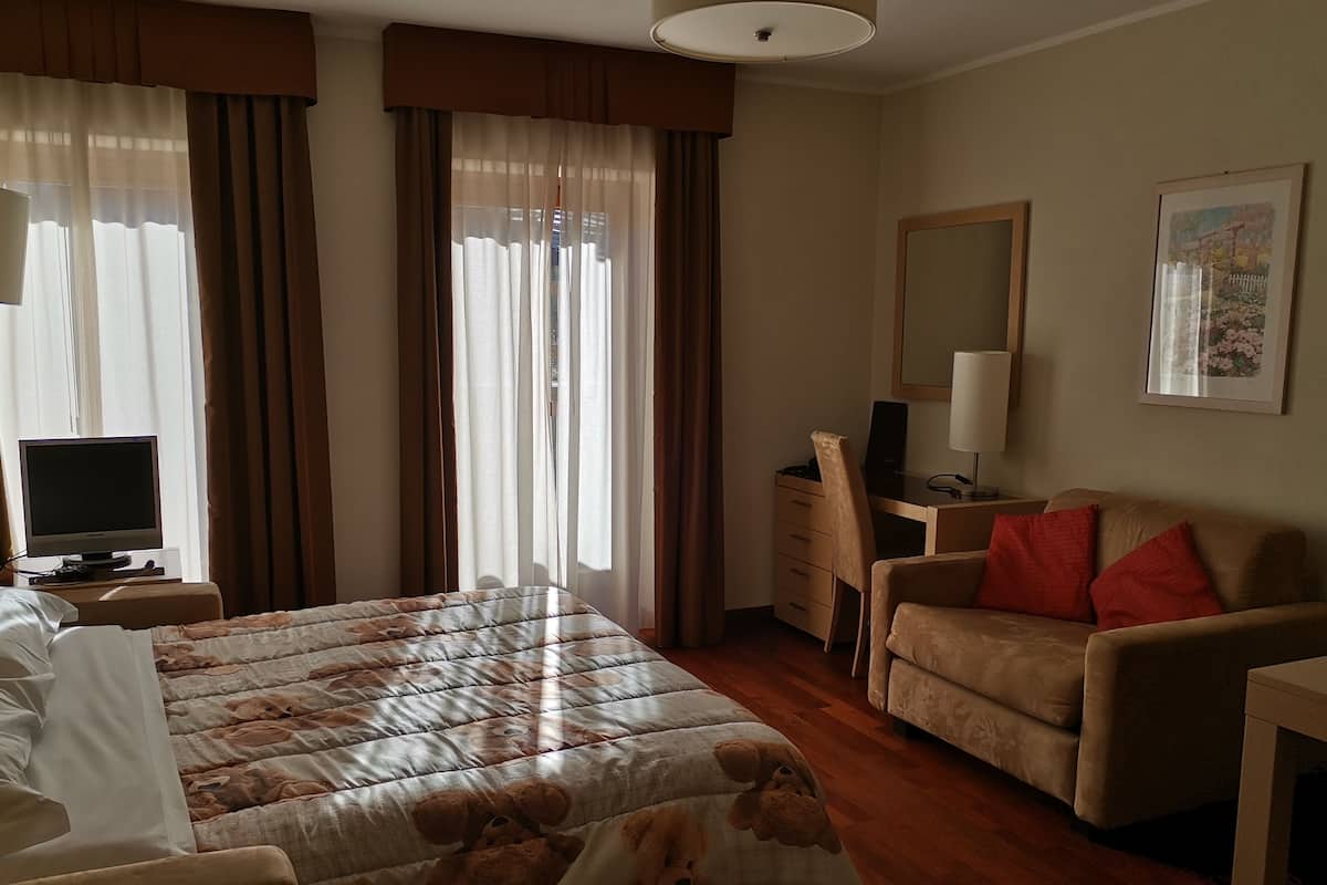 Une chambre d’hôtel avec un lit, un bureau, une chaise, une télévision et des rideaux.