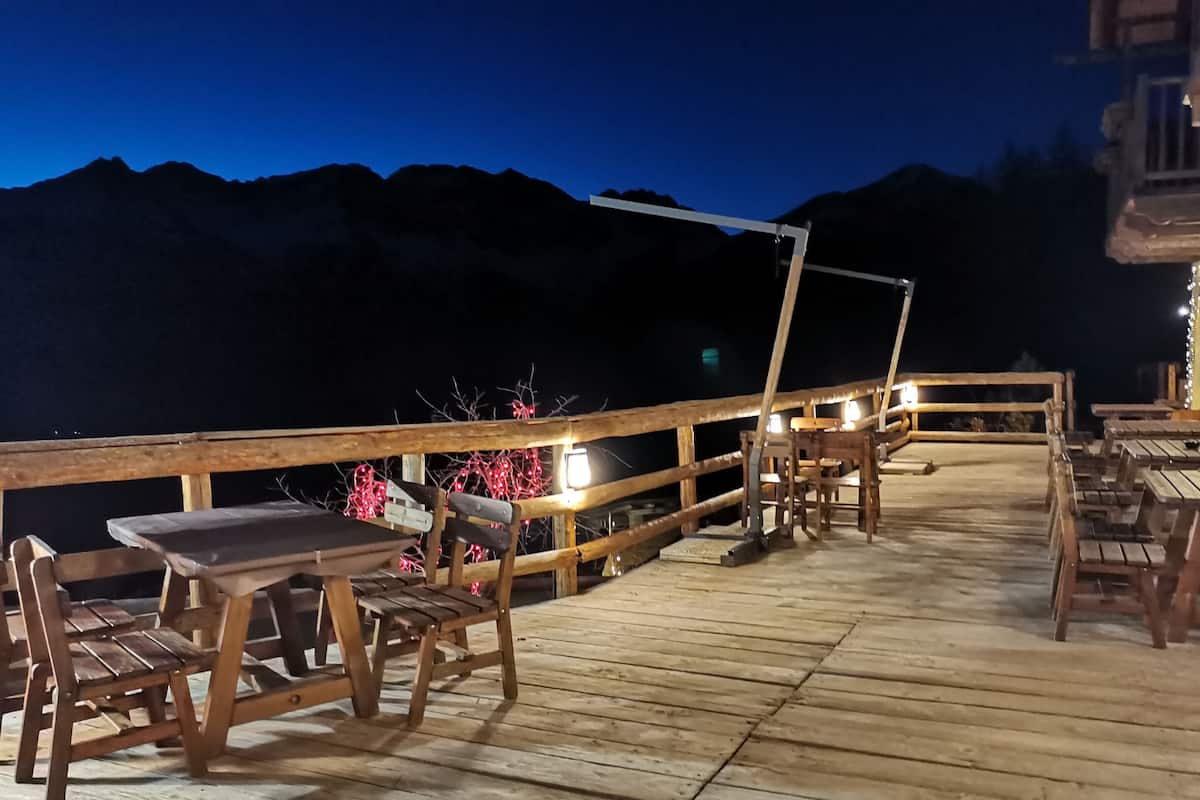 Une terrasse en bois, agrémentée de tables et de chaises, qui offre une vue sur un paysage montagneux la nuit.