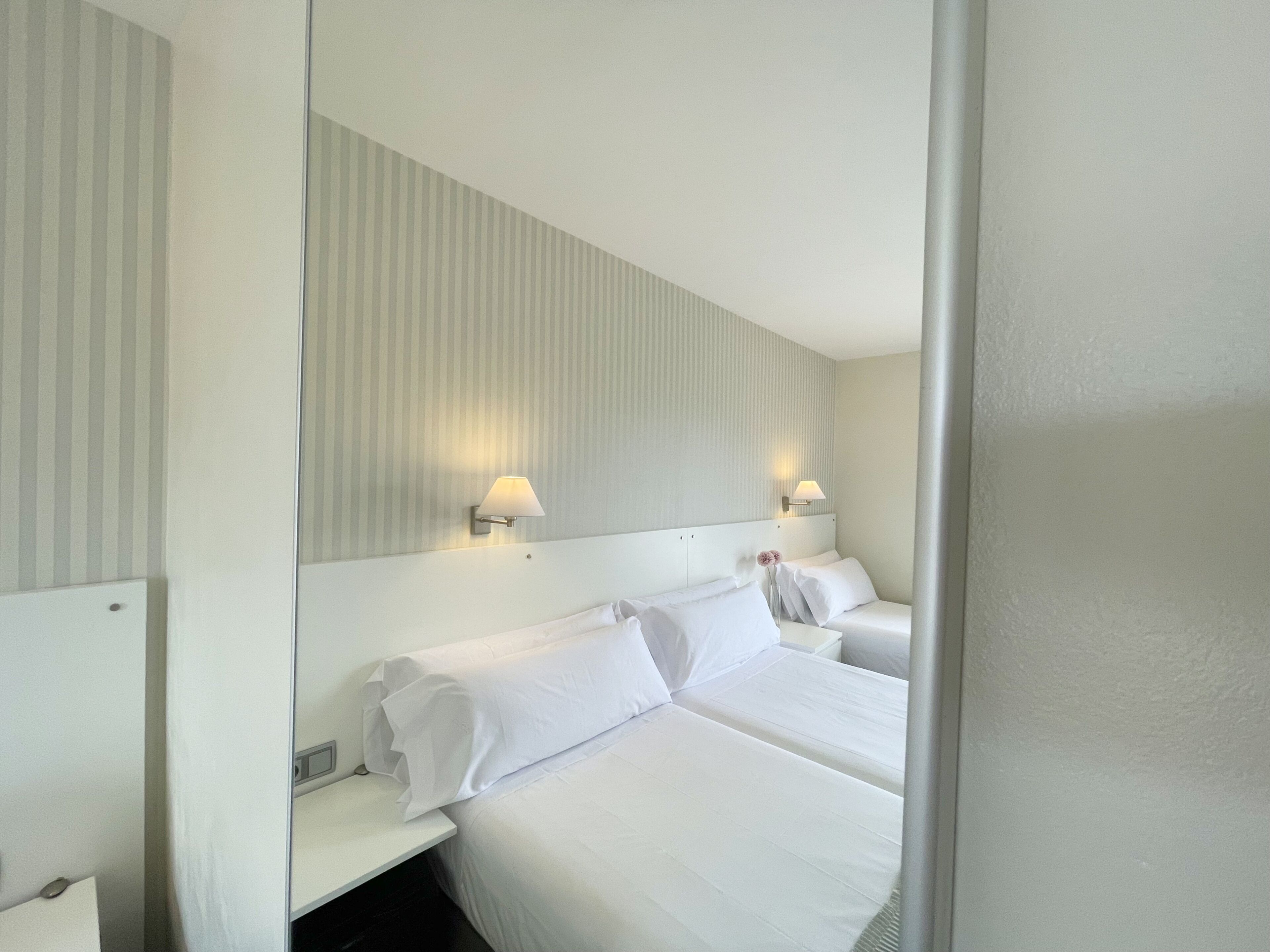 A hotel room with a large bed, two bedside tables, a mirror, and two wall-mounted lamps.