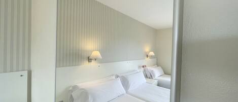 A hotel room with a large bed, two bedside tables, a mirror, and two wall-mounted lamps.