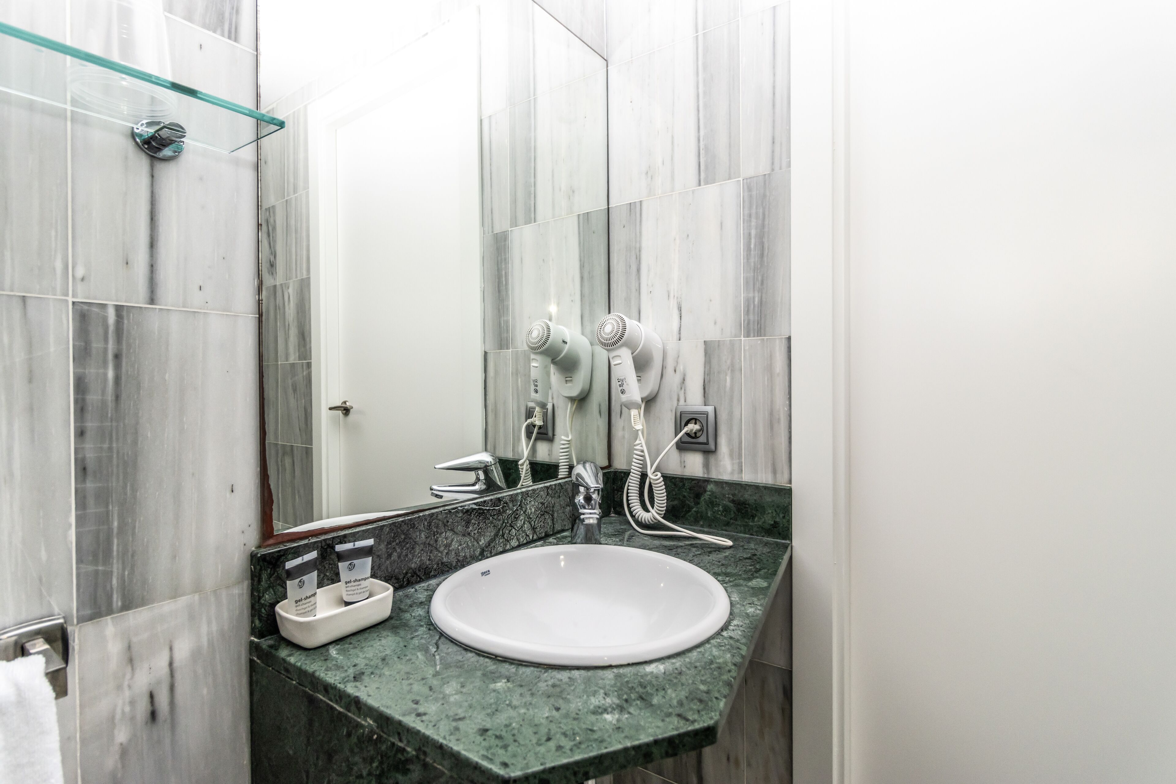 A bathroom with a white sink, a glass shower enclosure, and a marble-tiled shower area.