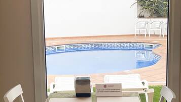 A view of a poolside area with a table and chairs, a sign with a logo, and a fence in the background.