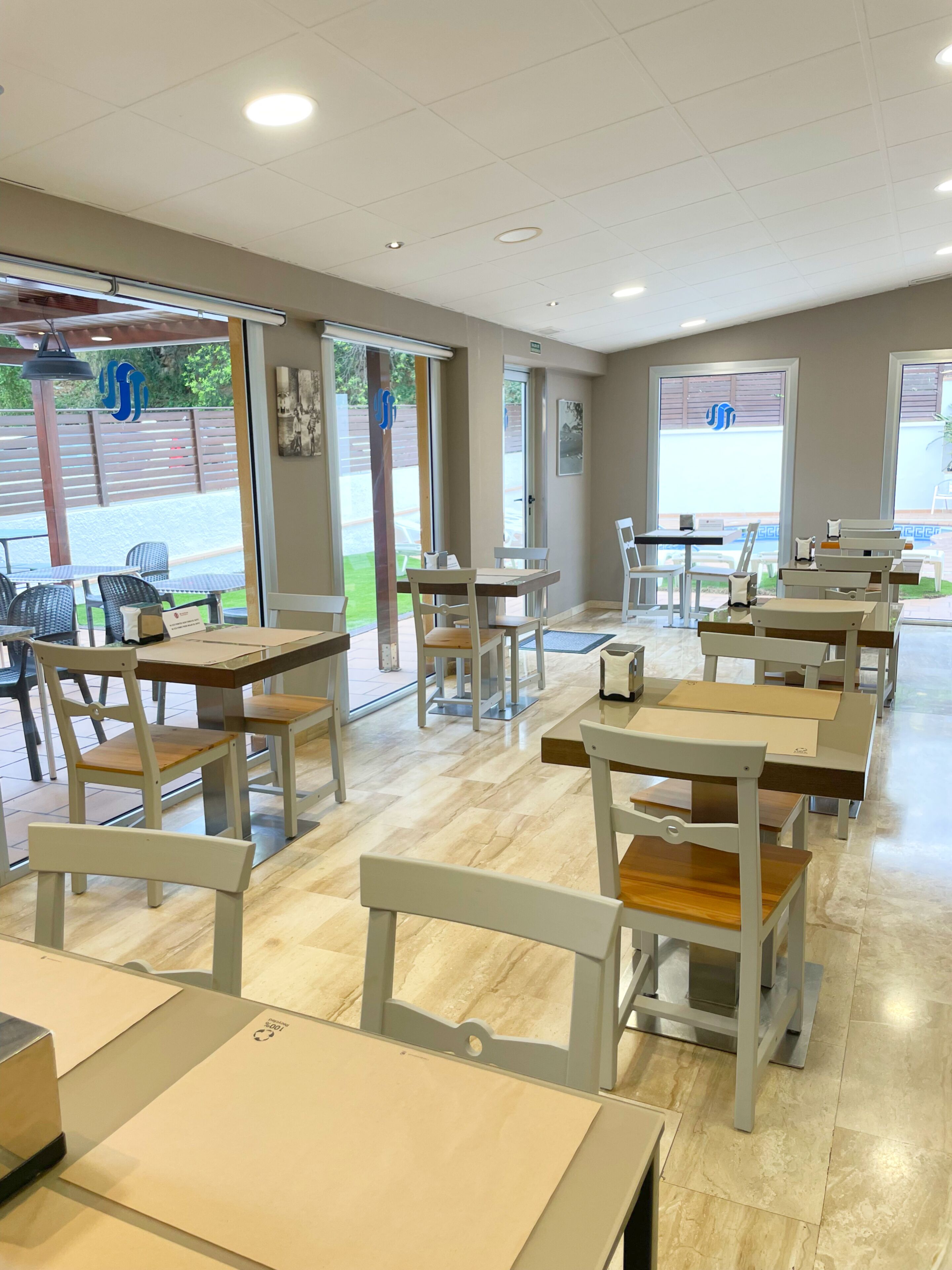 Un restaurante con mesas y sillas dentro, y vistas a través de puertas de cristal.